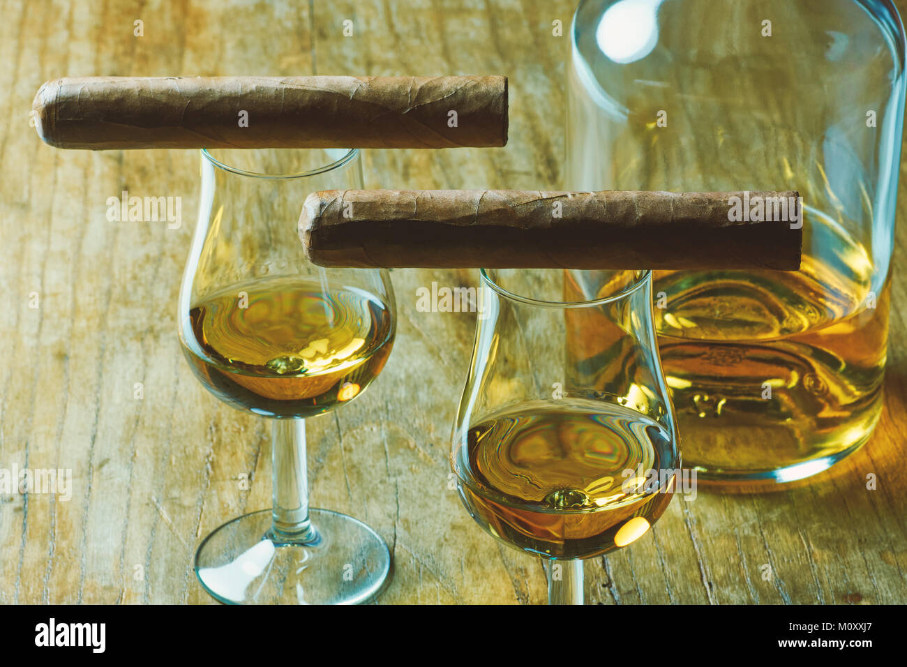 Nahaufnahme von Stillleben mit zwei Zigarre, eine Flasche Alkohol und zwei Glas Whiskey auf einem alten Holztisch, mit einem unscharfen Hintergrund Stockfoto