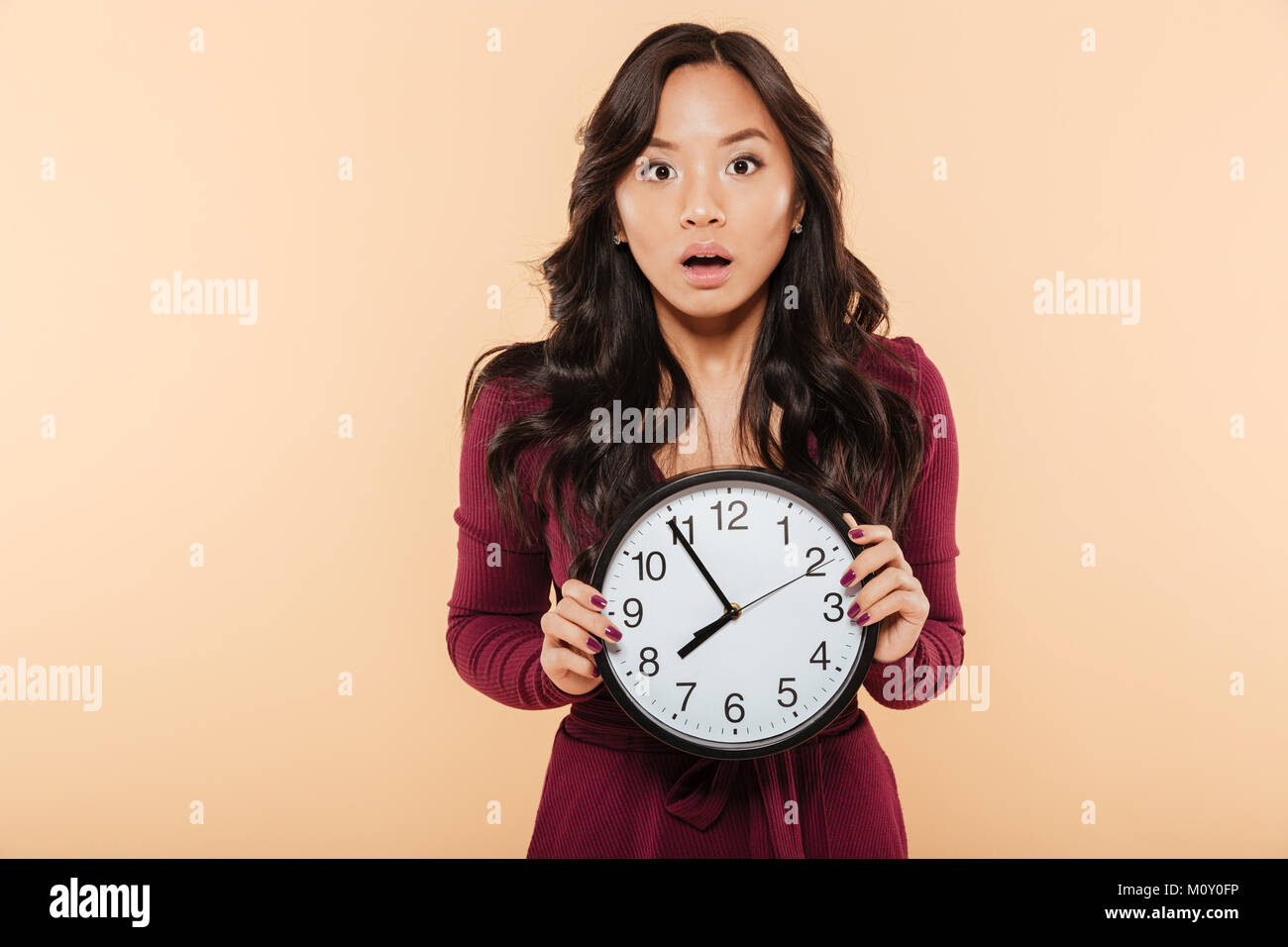 Junge asiatische Frau mit dem lockigen langen Haare, die Uhr zeigt fast 8, Ende, oder Fehlt etwas über Pfirsich Hintergrund Stockfoto