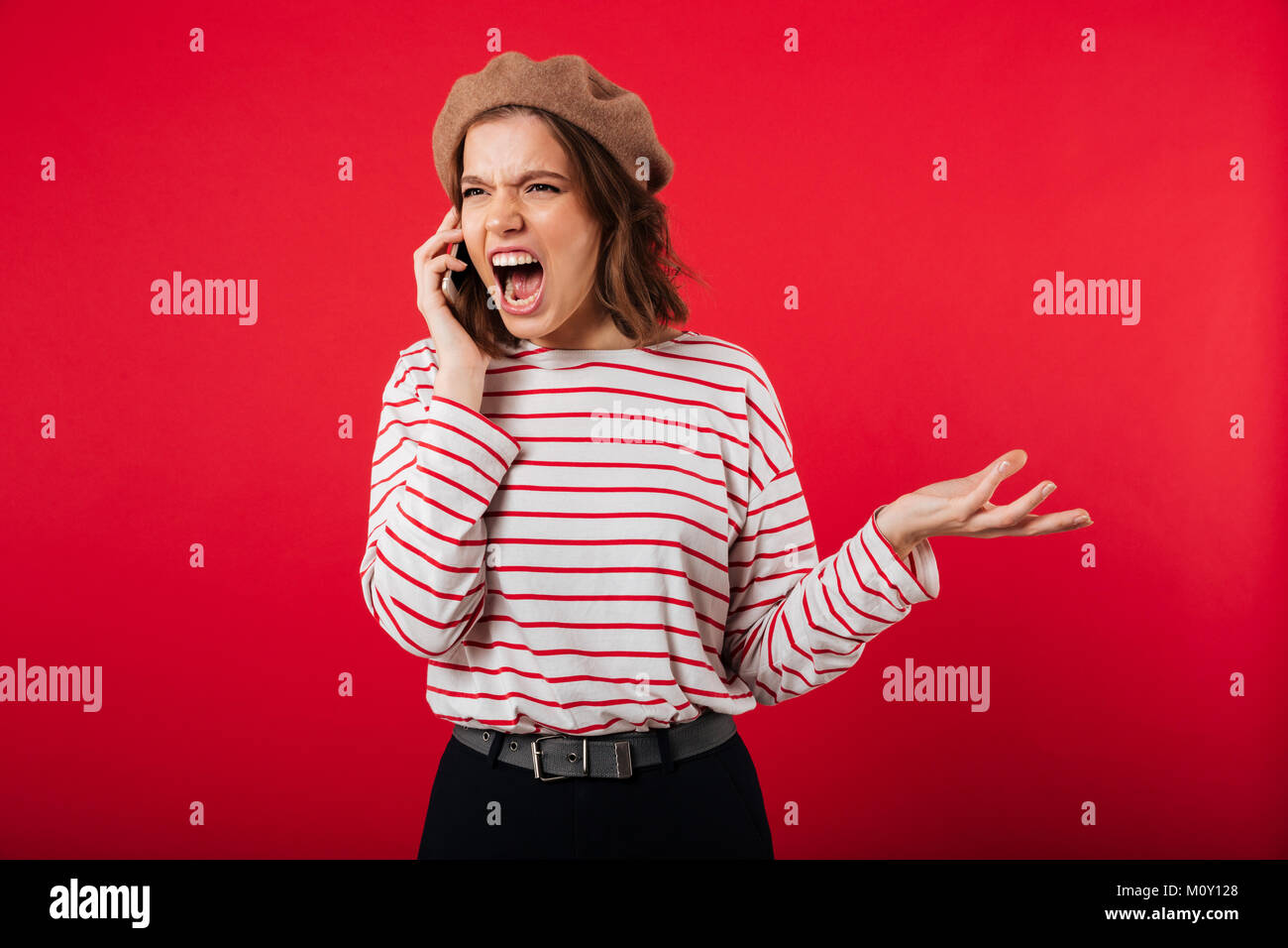 Porträt eines zornigen Frau mit beret Gespräch am Handy und Geschrei über rosa Hintergrund isoliert Stockfoto