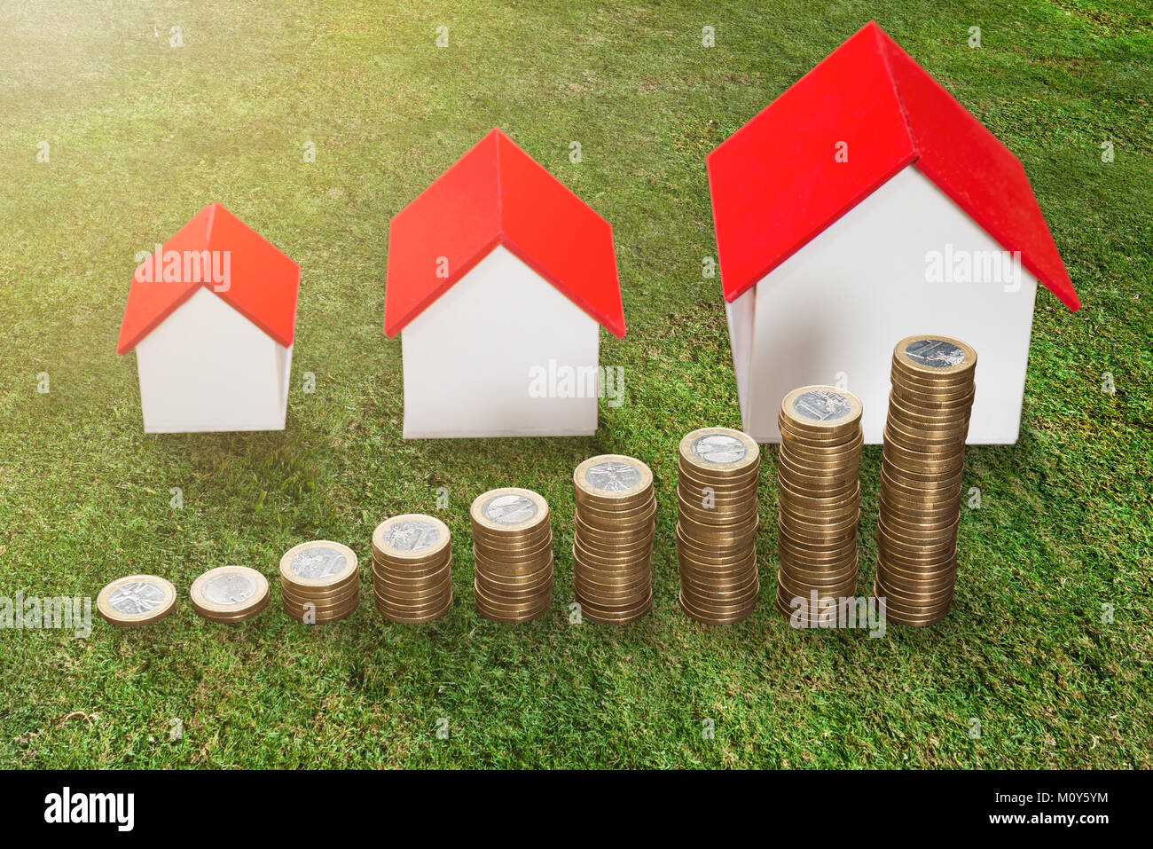 Stapel von zunehmenden Münzen Vor dem Haus Modell auf grünem Gras Stockfoto