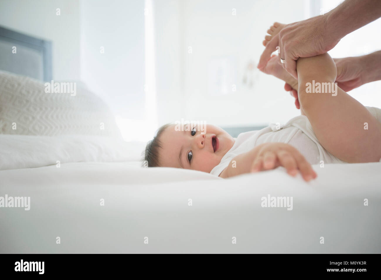 Vater holding Beine des Babys Sohn am Bett Stockfoto