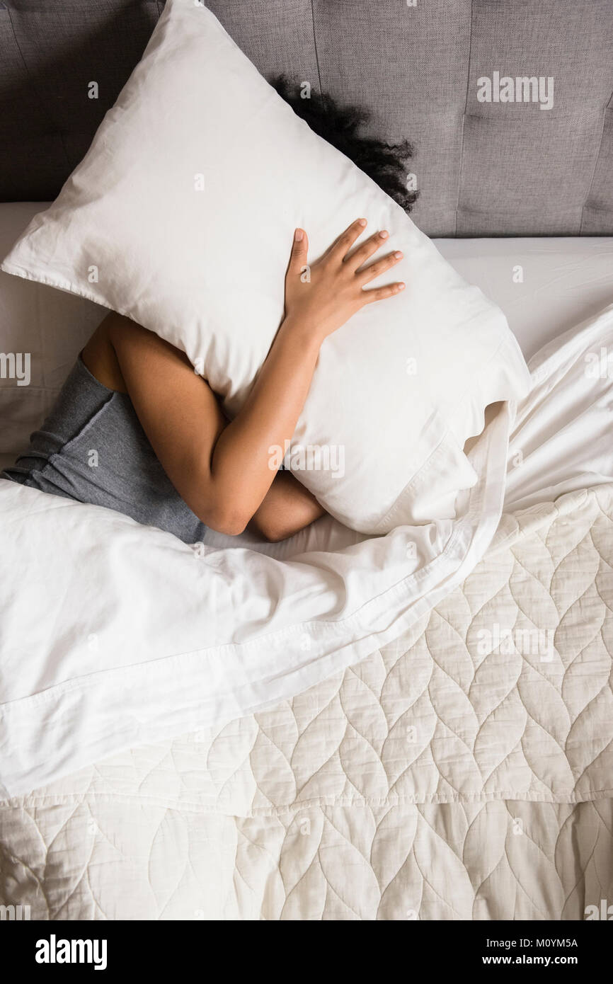 Afrikanische amerikanische Frau Festlegung auf dem Bett verstecken Gesicht unter dem Kopfkissen Stockfoto