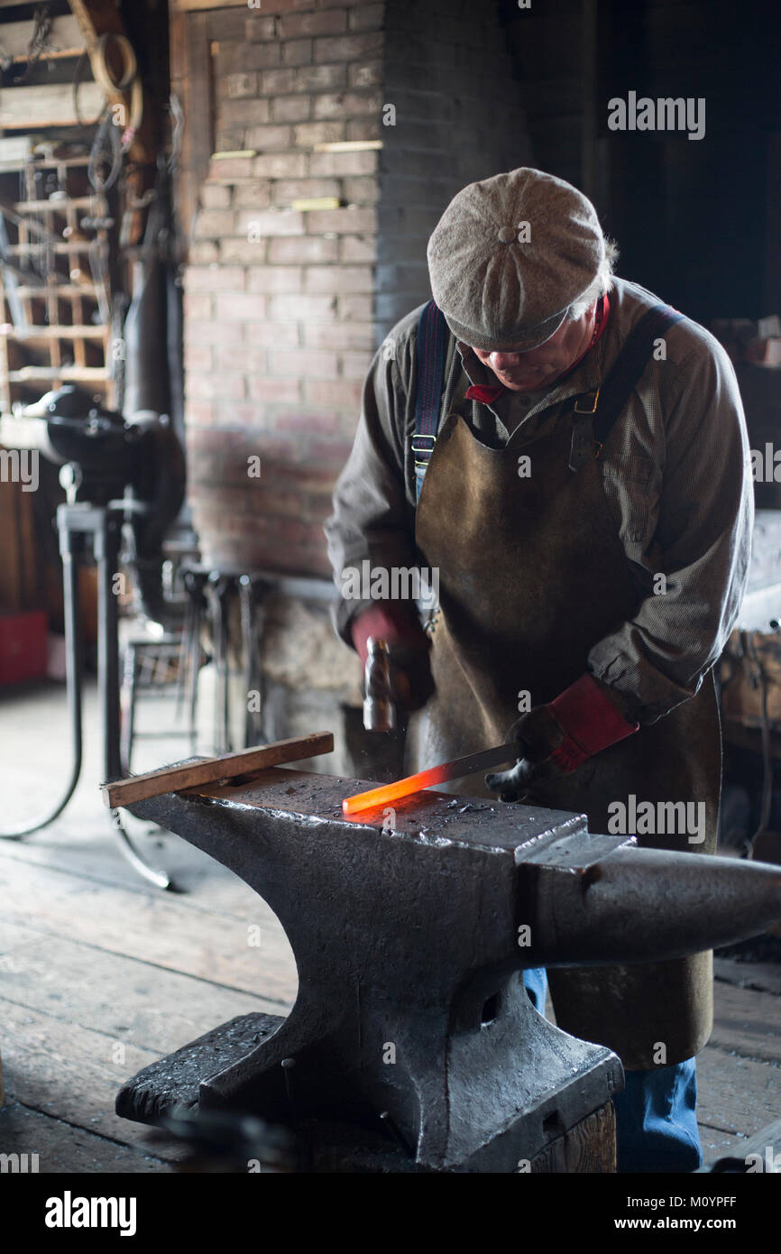 Schmied hämmert geschmolzenes Metall, um ein Hufeisen in Flett's Blacksmith Shop im Heritage Park Historical Village, Calgary, Alberta, Kanada zu schmieden Stockfoto