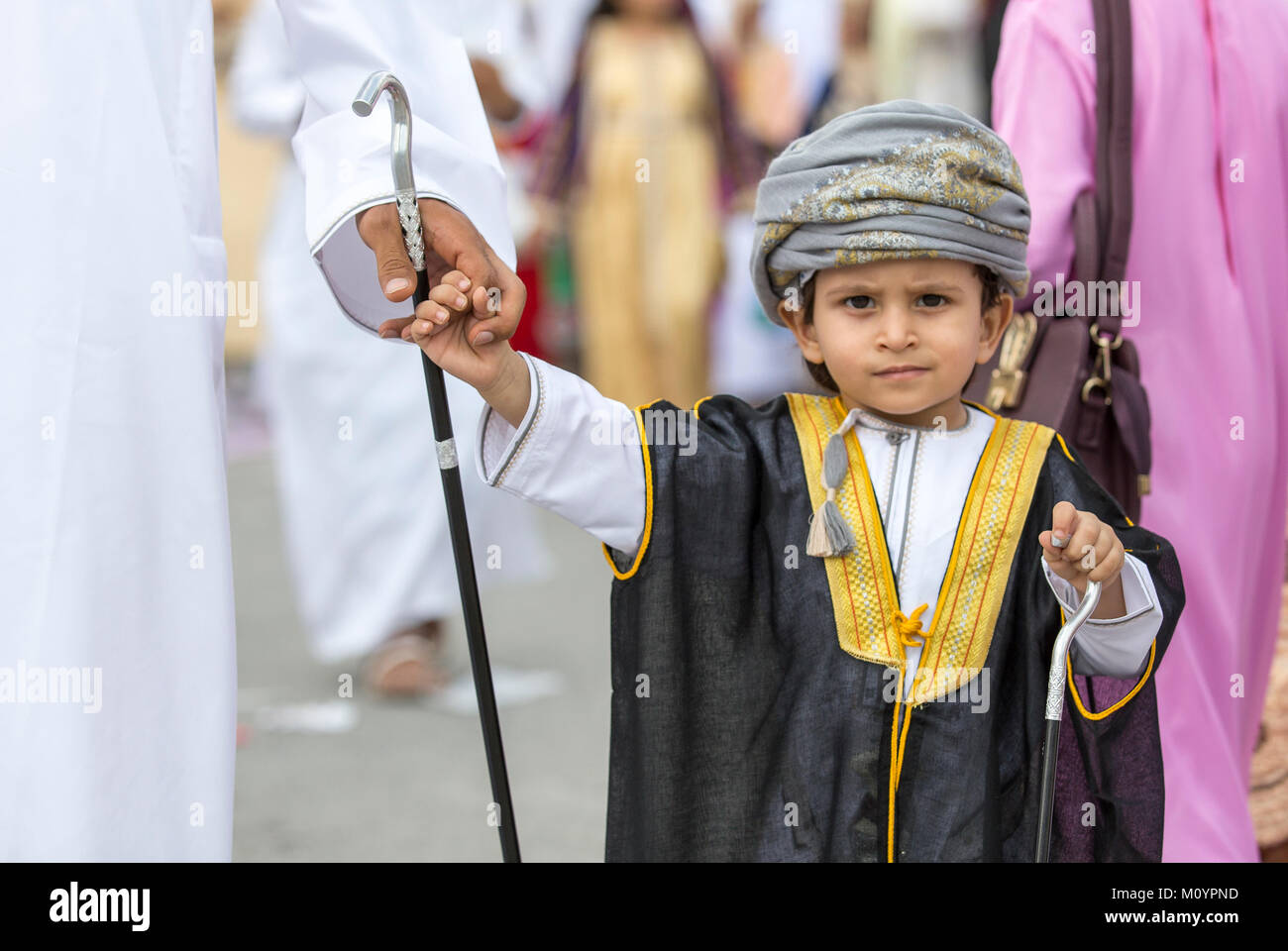 Nizwa, Oman - 26. Juni 2017: Der kleine Junge im traditionellen Outfit, Halten einer Hand seines Vaters an einem Spielzeug Markt an einem Tag des Eid al Fitr Stockfoto