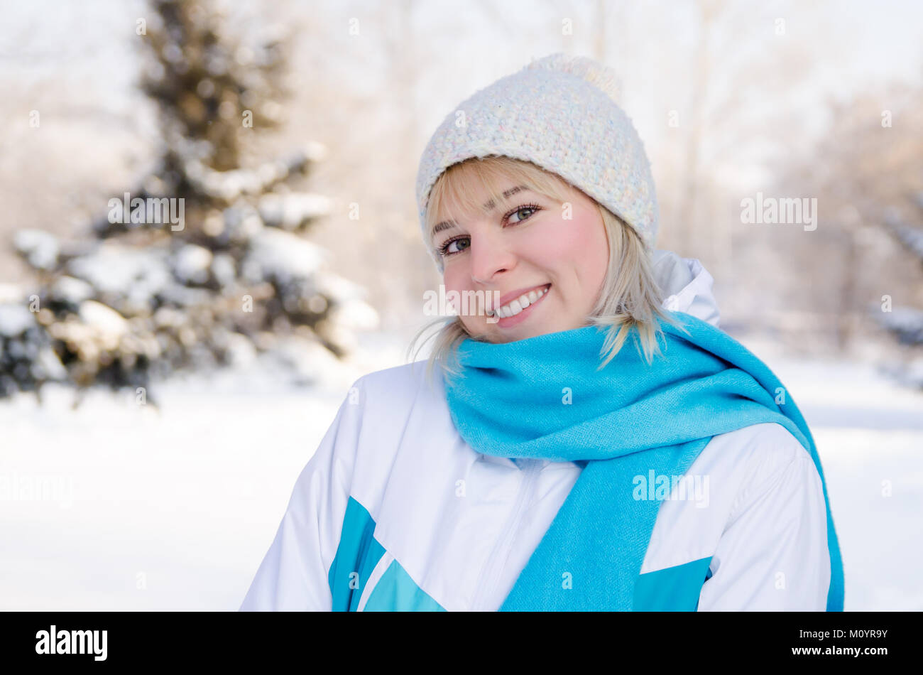 Portrait einer attraktiven Blondine lächelnde Mädchen in Sport Jacke und Hut in einem verschneiten Wald. Konzept Spaziergänge im Winter Forest für die Gesundheit. Stockfoto