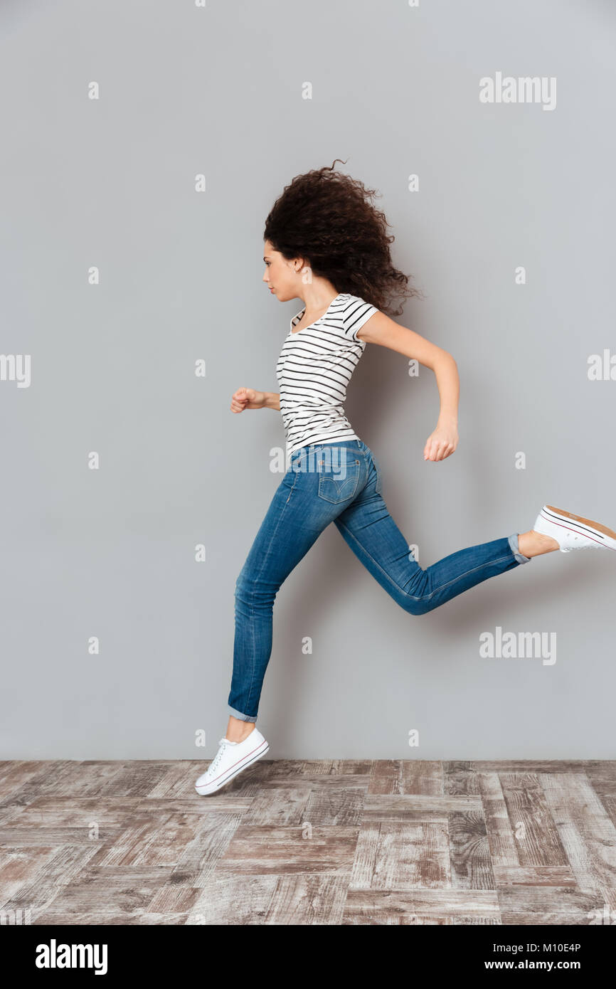 Lebhaft und motivierte Frau in gestreiften T-Shirt und Jeans, entlang graue Wand Gefühl Stärke Stockfoto