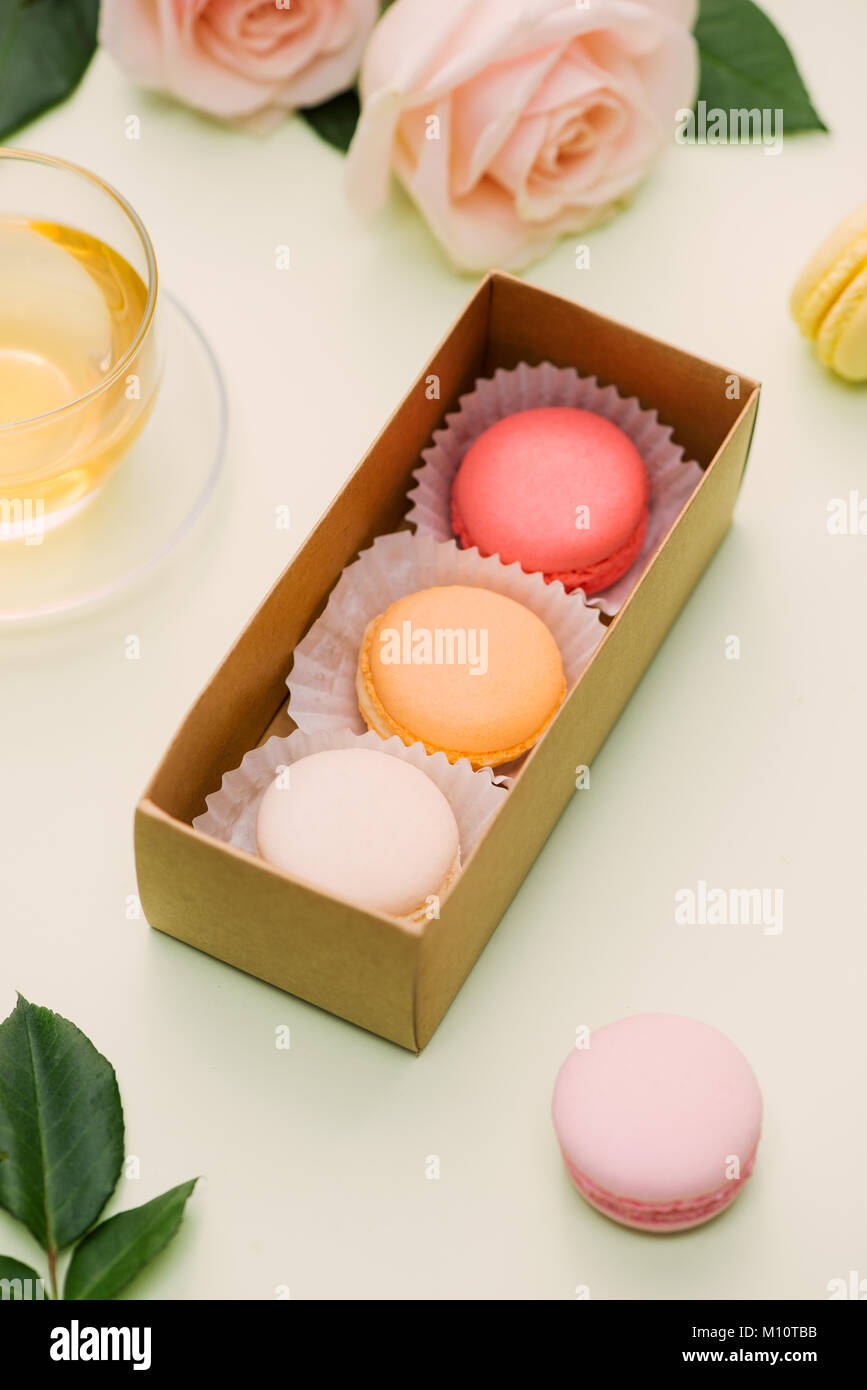 Bunte Makronen und rosa Blüten mit Tee auf hellgrün. Süße macarons in Geschenkbox. Ansicht von oben Stockfoto