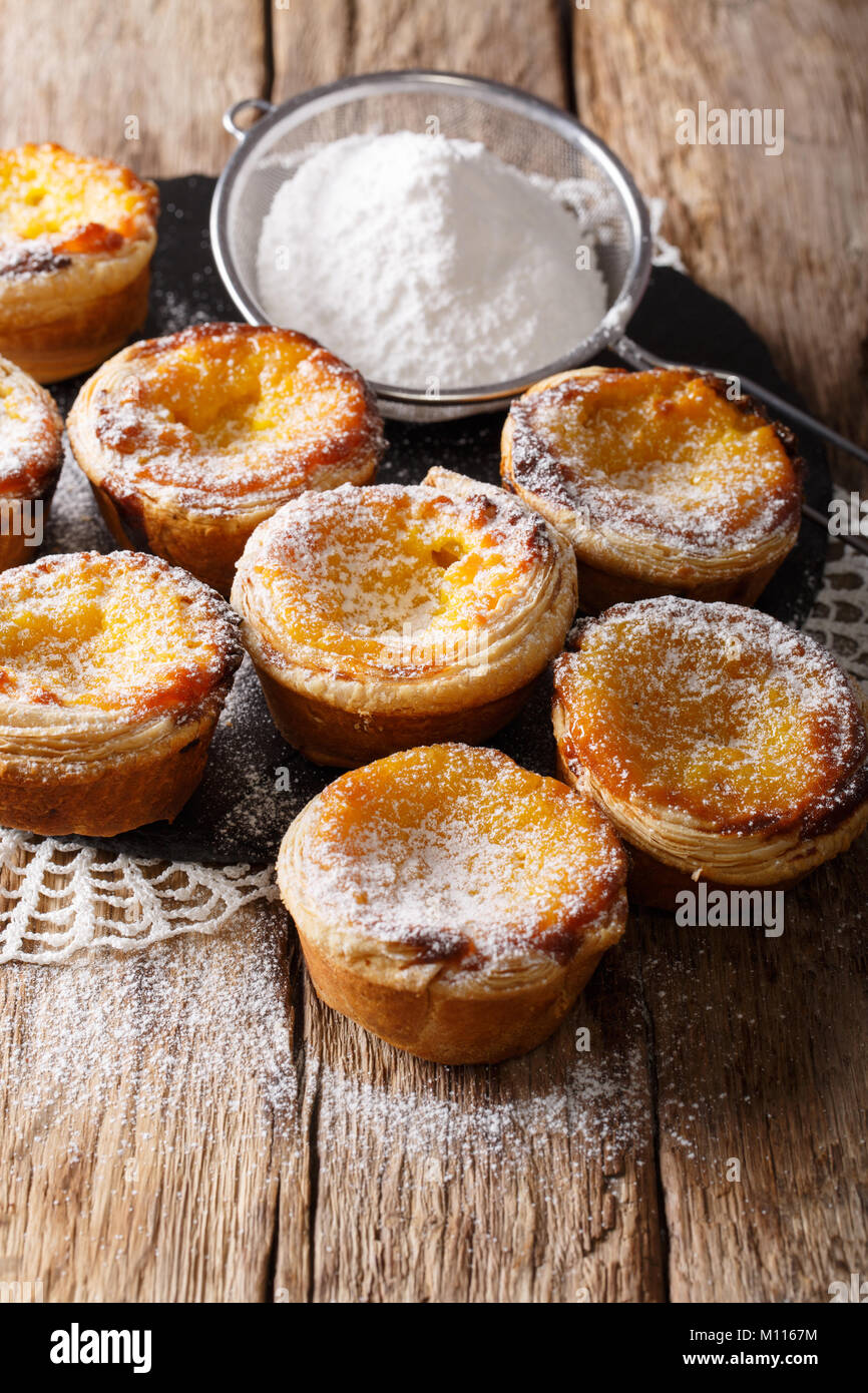 Hausgemachtes Gebäck: köstliche Pastel de nata mit Vanillesauce, bestreut mit Puderzucker close-up auf dem Tisch. Vertikale Stockfoto