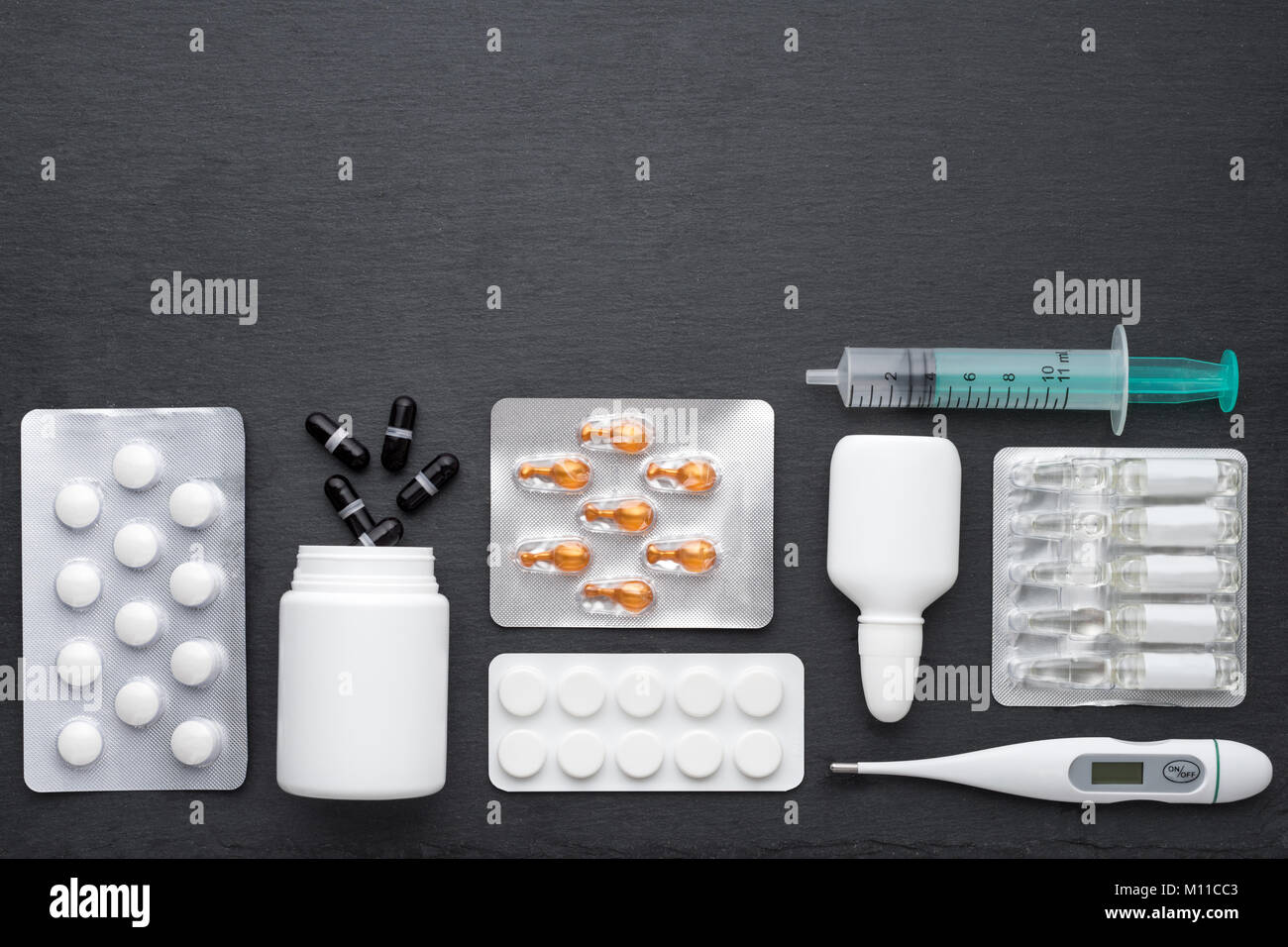 Thermometer, Nasentropfen Tabletten und Ampullen mit Medizin auf dunklem Schiefer. Ansicht von oben, flach, kopieren. Medikamente für die Behandlung und antibioti Stockfoto