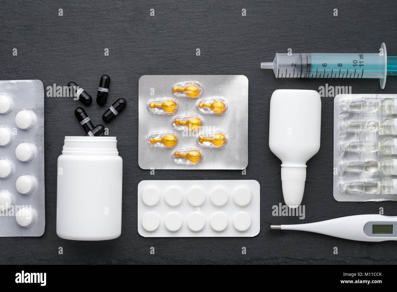 Thermometer, Nasentropfen Tabletten und Ampullen mit Medizin auf dunklem Schiefer. Ansicht von oben, flach. Medikamente für die Behandlung und Antibiotika, Gesundheit c Stockfoto