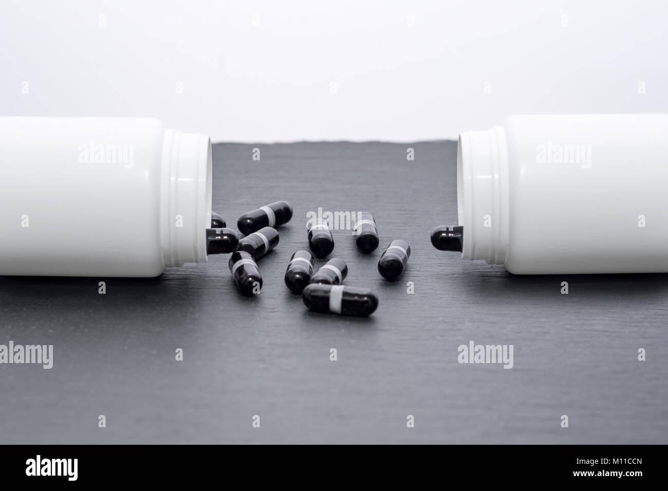 Schwarz Ergänzung Kapseln sind von den weißen Flaschen auf schiefer Board gegossen. Medizin, Gesundheitswesen Konzept Stockfoto