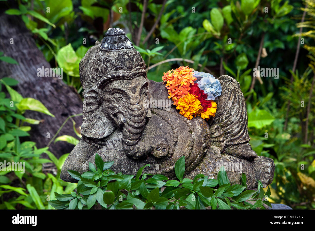 Indonesien, Insel Bali, in der Nähe von tejakula Dorf, Gaia Oasis Resort. Statue des hinduistischen Gottes Ganesha mit Blume im Garten. Stockfoto