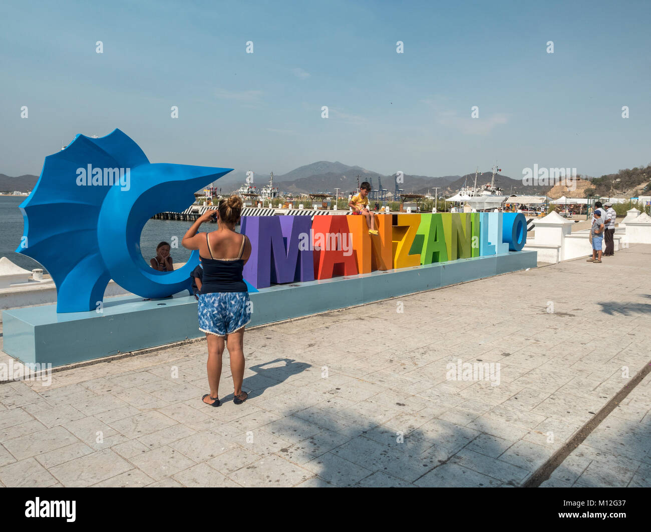 Eine Familie posieren für Fotos an der Manzanillo bunte Touristische Schild mit Blauer Fächerfisch auf der Uferpromenade von Manzanillo Colima Mexiko Stockfoto