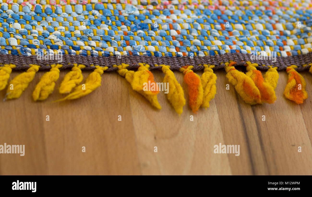 Bunte gelb orange Fringe mit Quasten am Rande einer Wolldecke oder gesponnene Wolle Textil mit natürlichen Fasern liegen auf einem Holz- Oberfläche Stockfoto