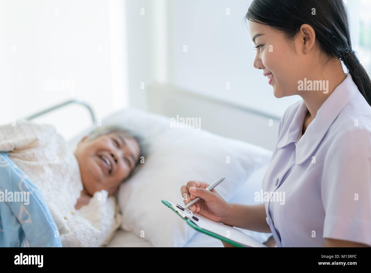 Asiatische Krankenschwester und kontrollieren die Geschichte der Krankheit ältere Patienten im Bett lag. Krankenschwester kümmert sich um eine ältere Frau. Stockfoto