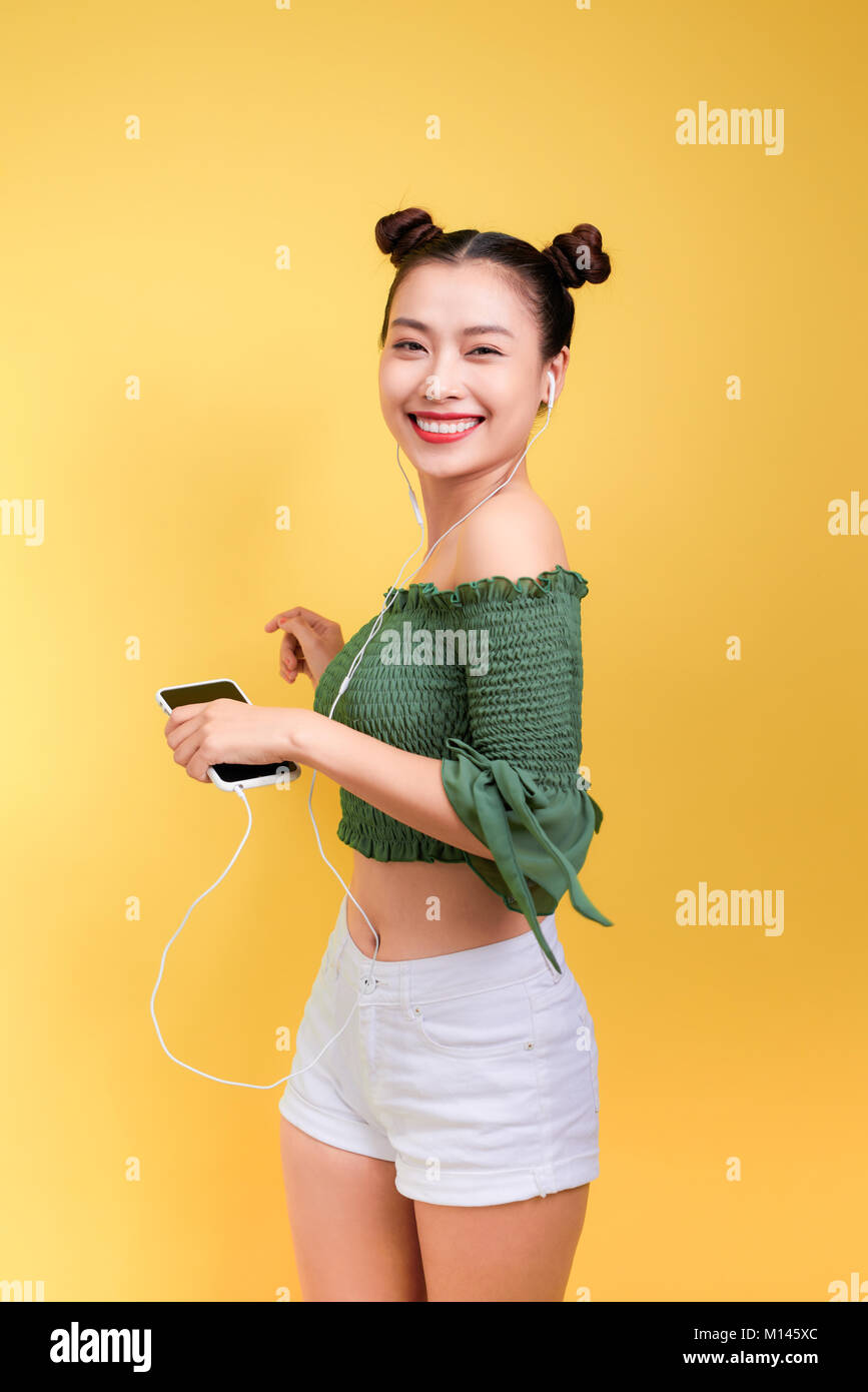 Mode lächelt asiatische Frau hören die Musik im Kopfhörer auf gelbem Hintergrund Stockfoto
