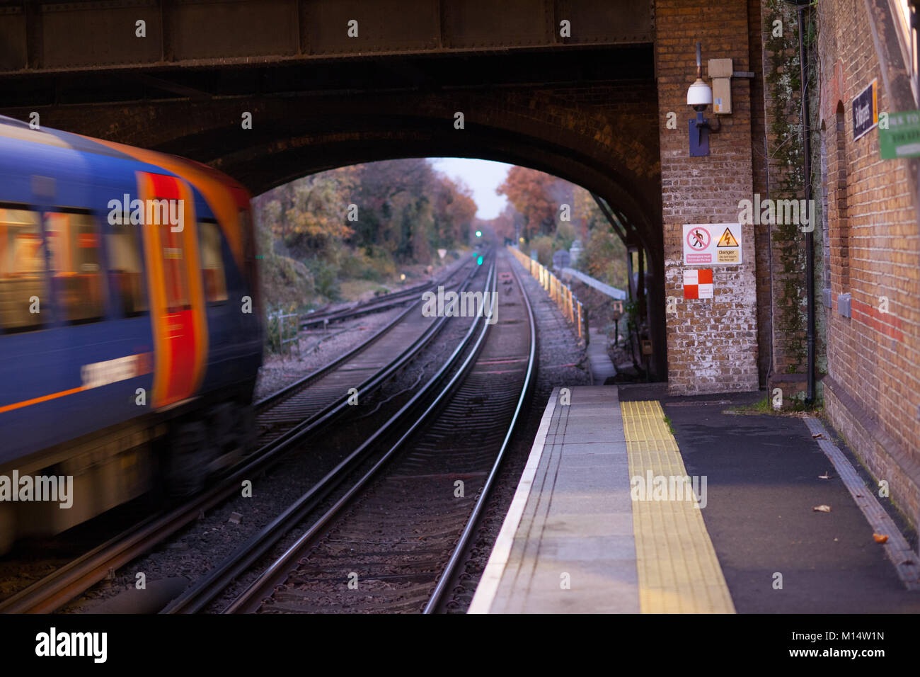 Ein südwestliches Rail Zug Geschwindigkeiten, mit der Wirkung von Bewegungsunschärfe. Backsteinmauer und Warnzeichen sind scharf. St Margrets, Richmond, England Stockfoto