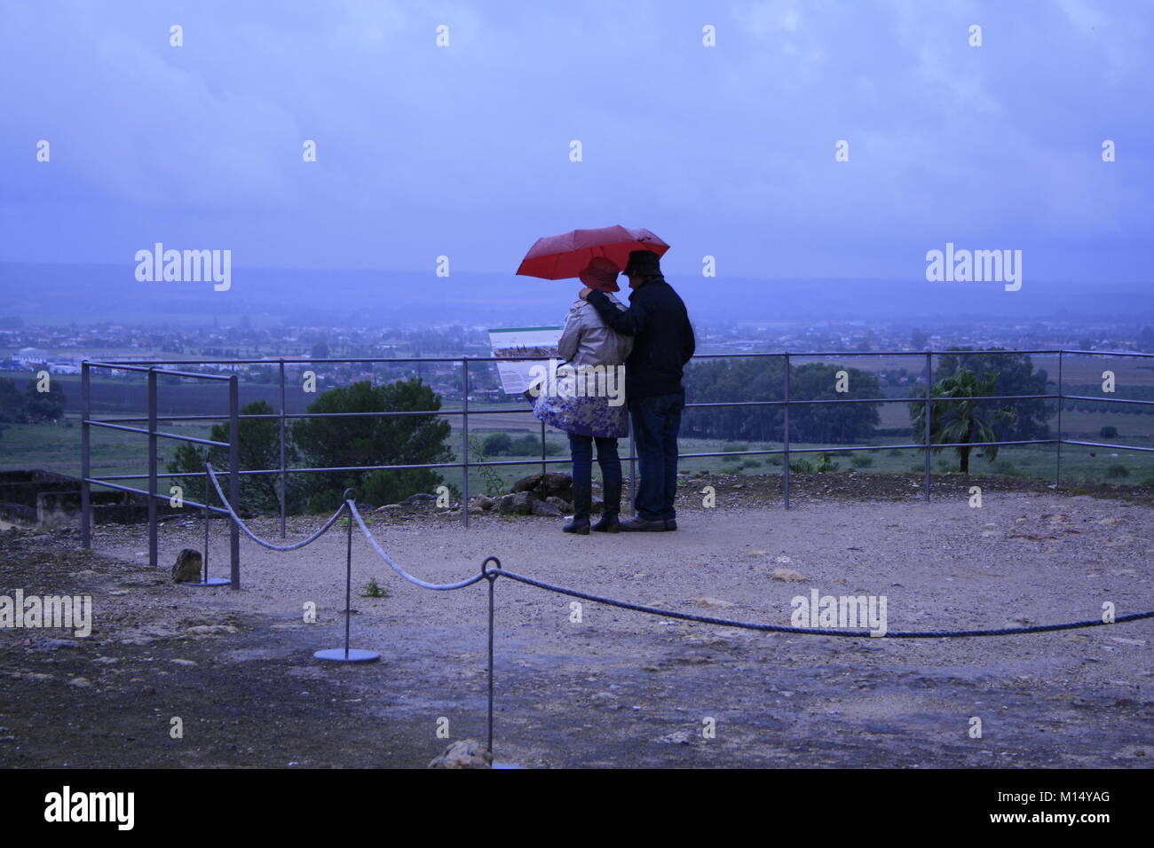 Ein Paar in einem regnerischen Tag mit roten Regenschirm in Madinat azahra, Cordoba, Spanien Stockfoto