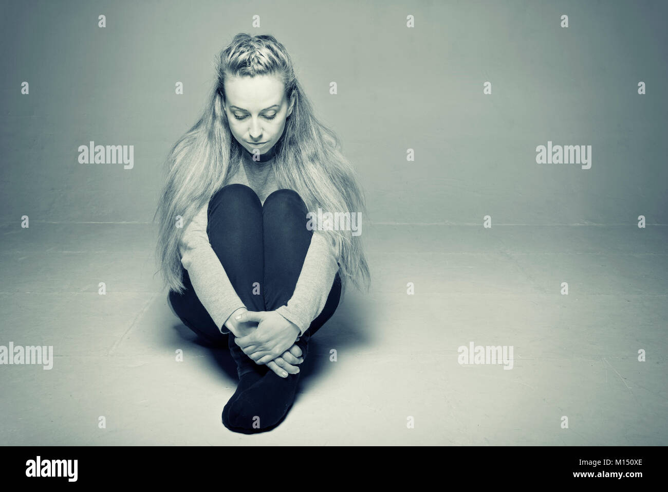Traurig, deprimiert Frau im leeren Raum auf dem Boden sitzen, die Hände um die Beine nach unten getonten Bild gewickelt Stockfoto