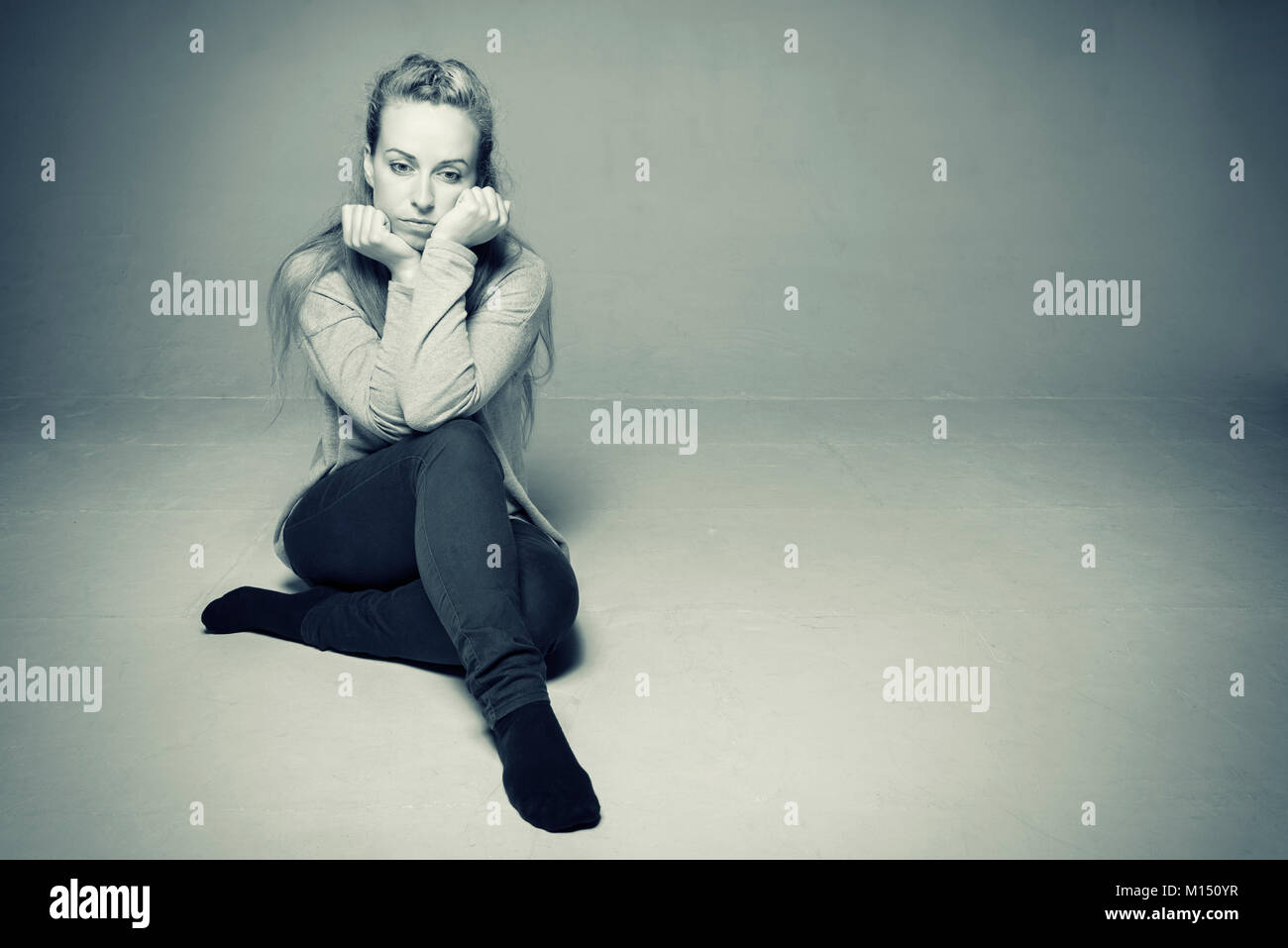 Traurige Frau im leeren zimmer sitzen auf dem Boden Ellenbogen ruhend auf gebogenem Knie Gesicht zwischen geballten Hände traurig und entfernten getonten Bild gedrückt Stockfoto