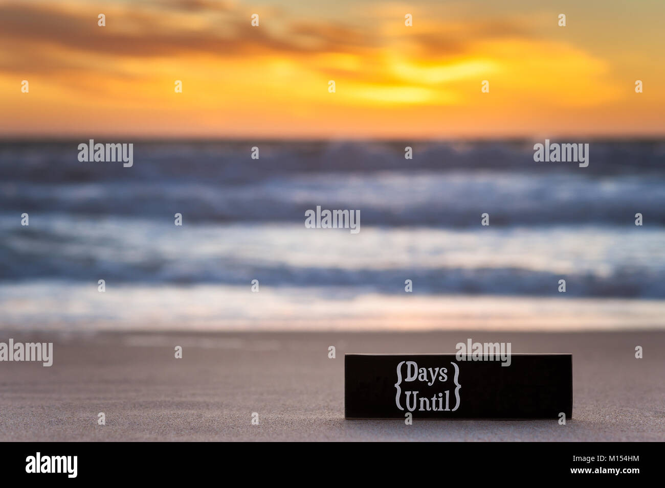 Horizontale Foto von einem Countdown Kalender Schwarzes Brett Zeichen am Strand mit pazifischen Ozean im Hintergrund bei Sonnenuntergang. Stockfoto