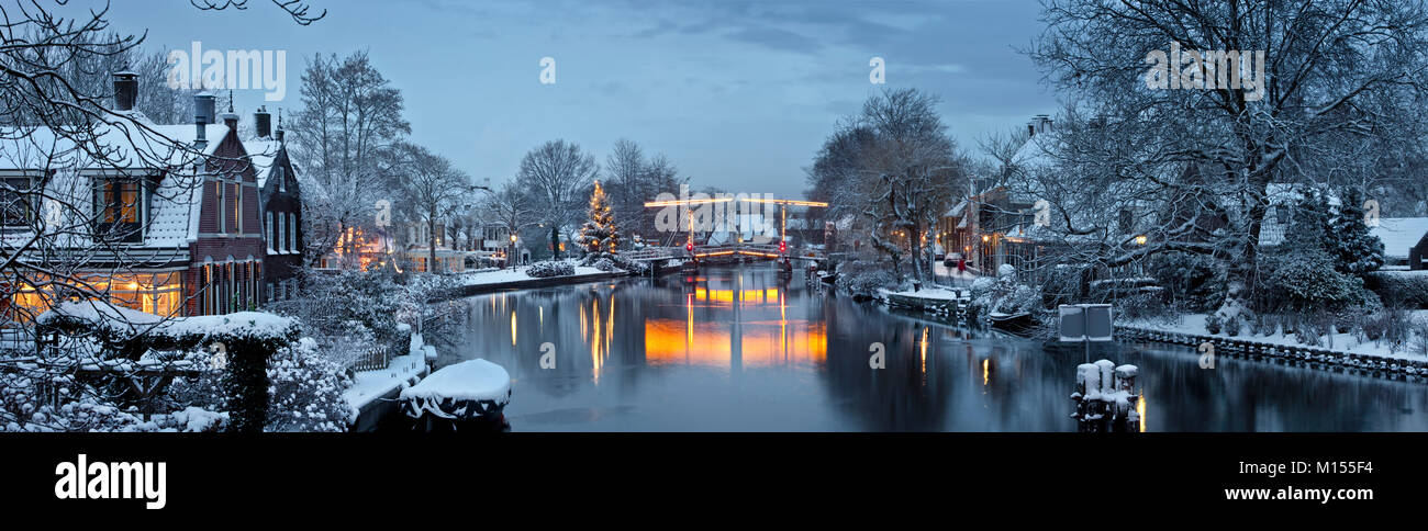 Die Niederlande, Vreeland, Weihnachtsbaum und beleuchtete Zugbrücke über den Fluss genannt: Vechte. Dämmerung. Winter, Schnee. Panoramablick. Stockfoto