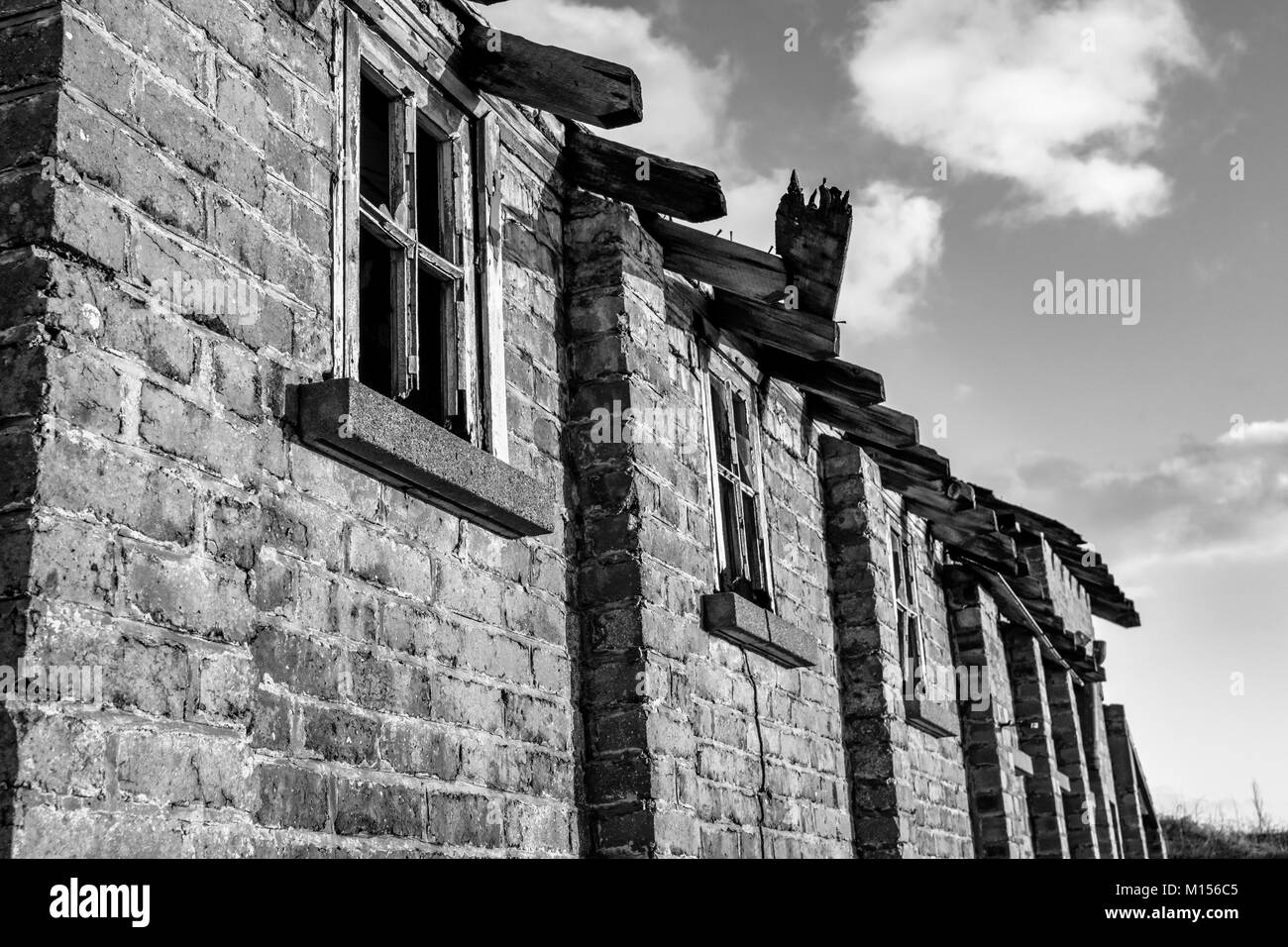 Schwarz-weiß Foto von einem alten Backsteingebäude mit kaputten Fenstern Stockfoto