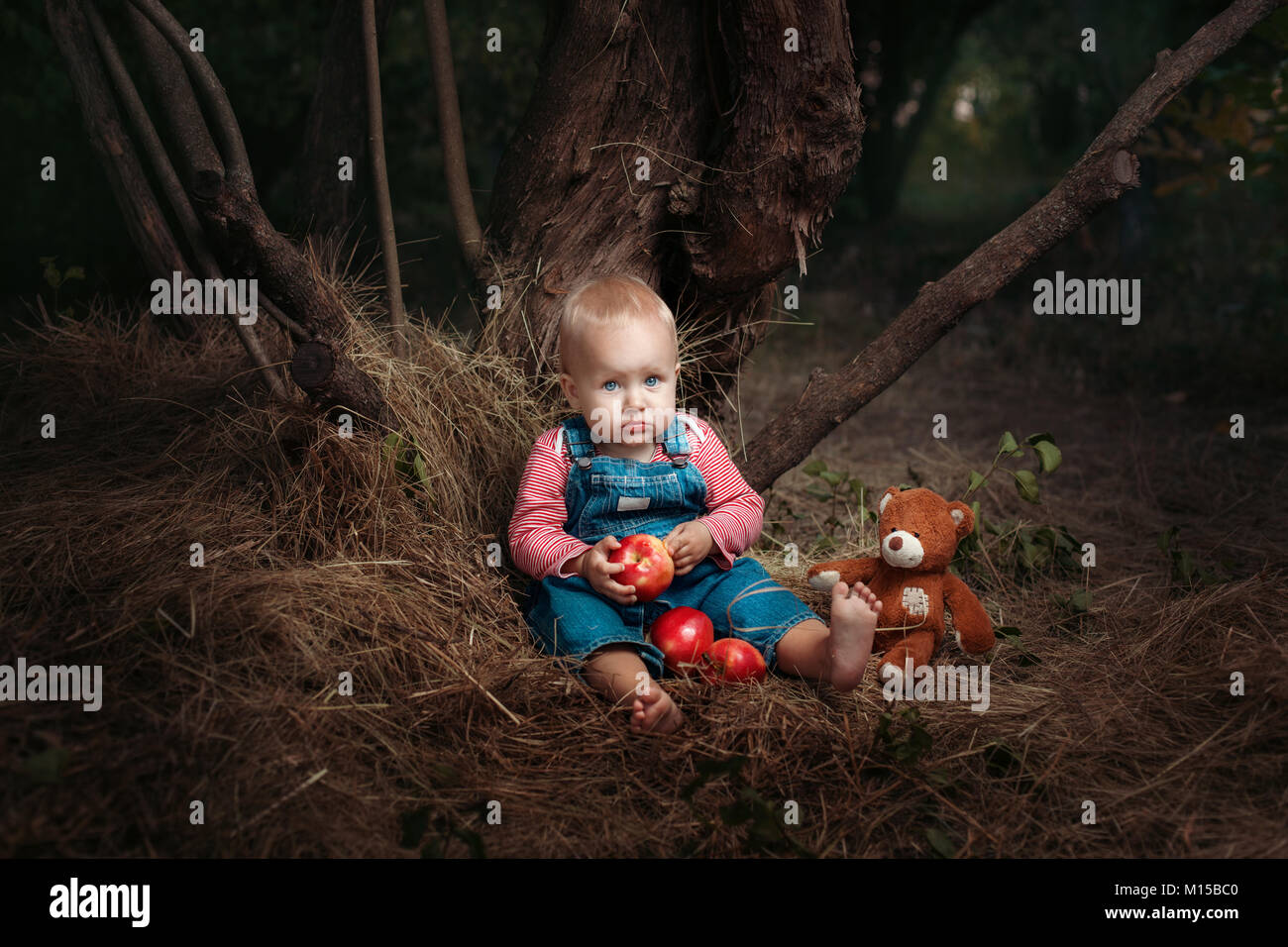 Kleines Mädchen mit einem Spielzeug Teddy saß unter einem Baum. Stockfoto