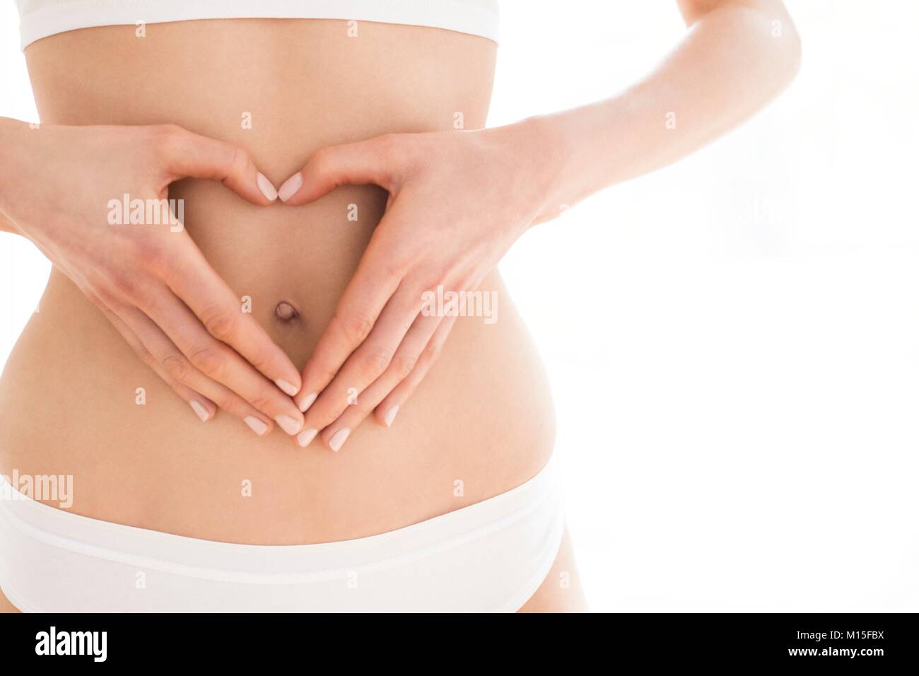 MODEL RELEASED. Junge Frau mit Händen in Herz Form auf den Bauch. Stockfoto