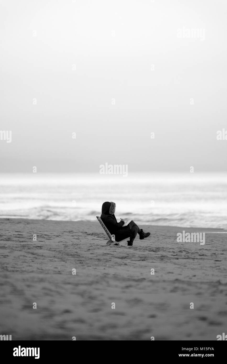 Eine Person, die am Strand eines Wintermeers ein Buch liest Stockfoto