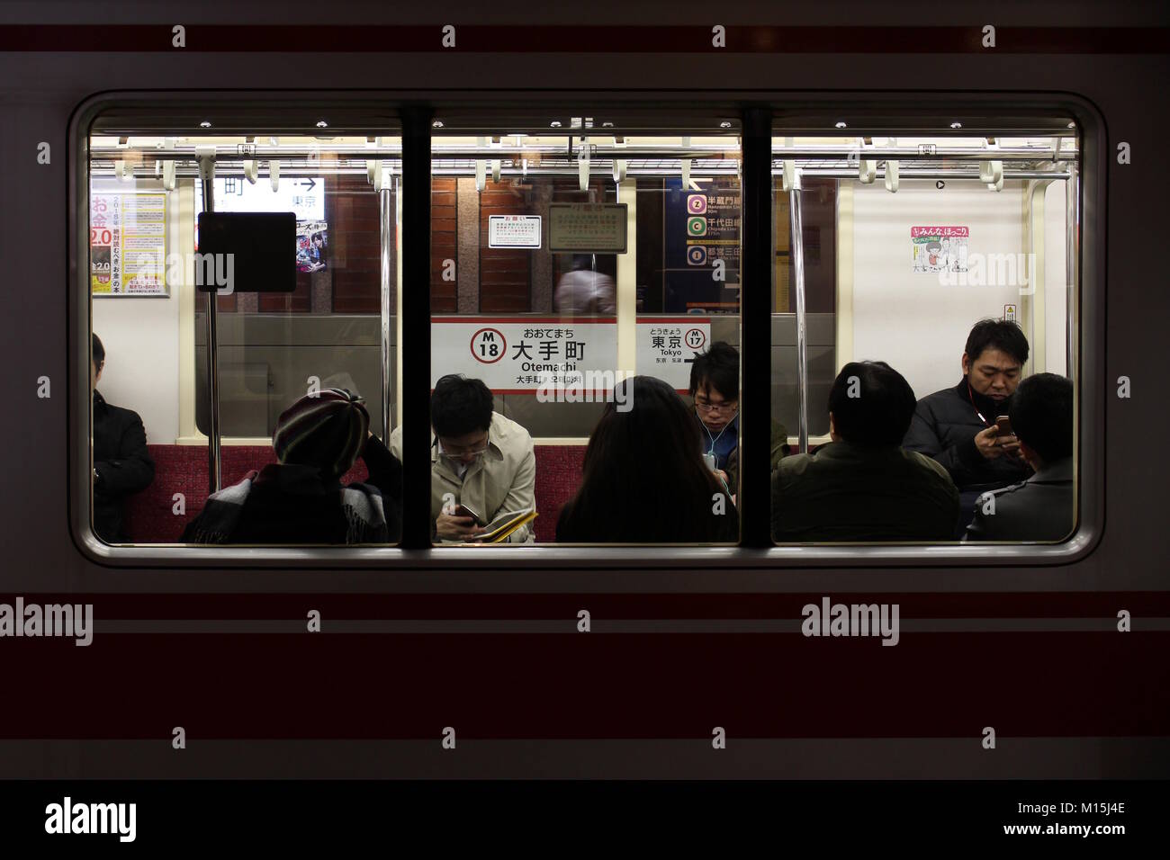 Blick durch das Fenster in das Innere der Marunouchi Linie Zug an Otemachi Station in den frühen Abend mit Fahrgäste, die ihre Telefone. Stockfoto
