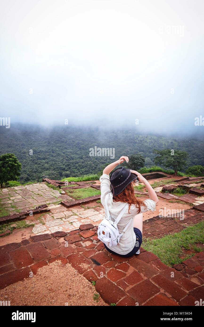 Rothaarige Mädchen in Hut sitzt oben Sigiriya Felsen, Sri Lanka. Ansicht von hinten Stockfoto