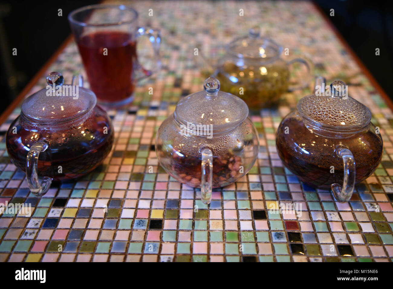 Bunte Bild mit Glas Teekanne mit heißem Obst Tee Getränken gefüllt auf einem Mosaik quadratischen Muster Tischplatte mit einem Gegossenen fertig zu haben. Stockfoto