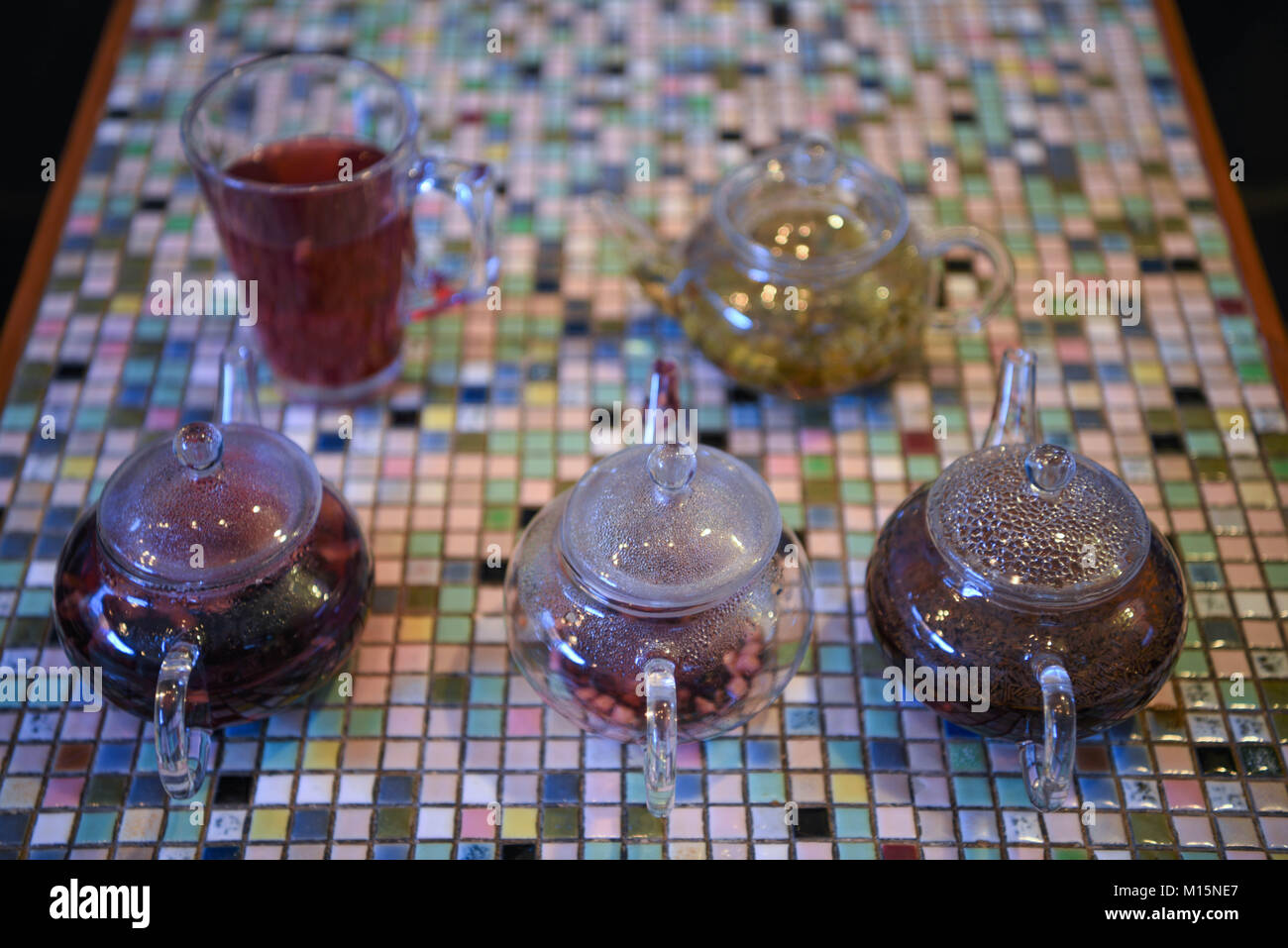 Bunte Bild mit Glas Teekanne mit heißem Obst Tee Getränken gefüllt auf einem Mosaik quadratischen Muster Tischplatte mit einem Gegossenen fertig zu haben. Stockfoto