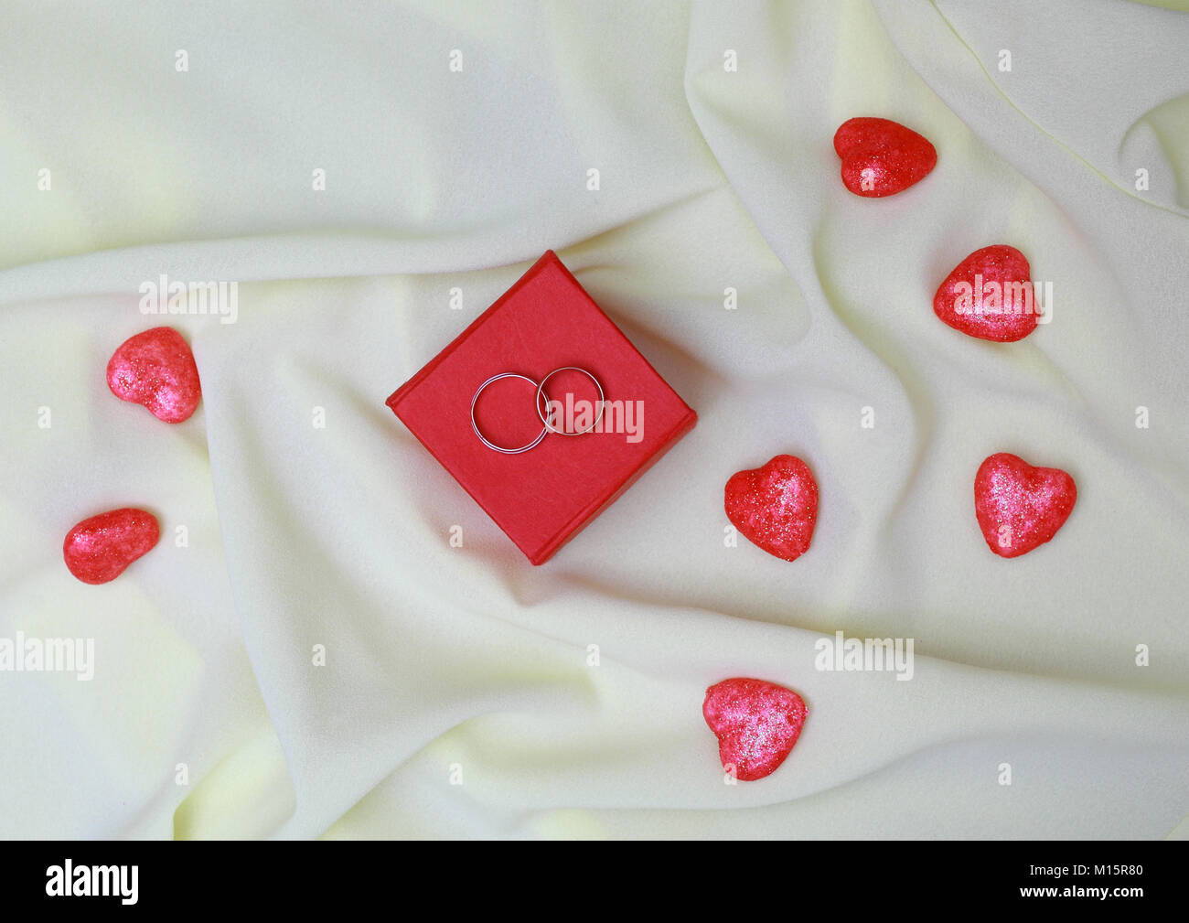 Leichte Seide plissiert Red Box. Es gibt zwei Trauringe. In der Nähe befindet sich eine Menge von Herzen. Stockfoto