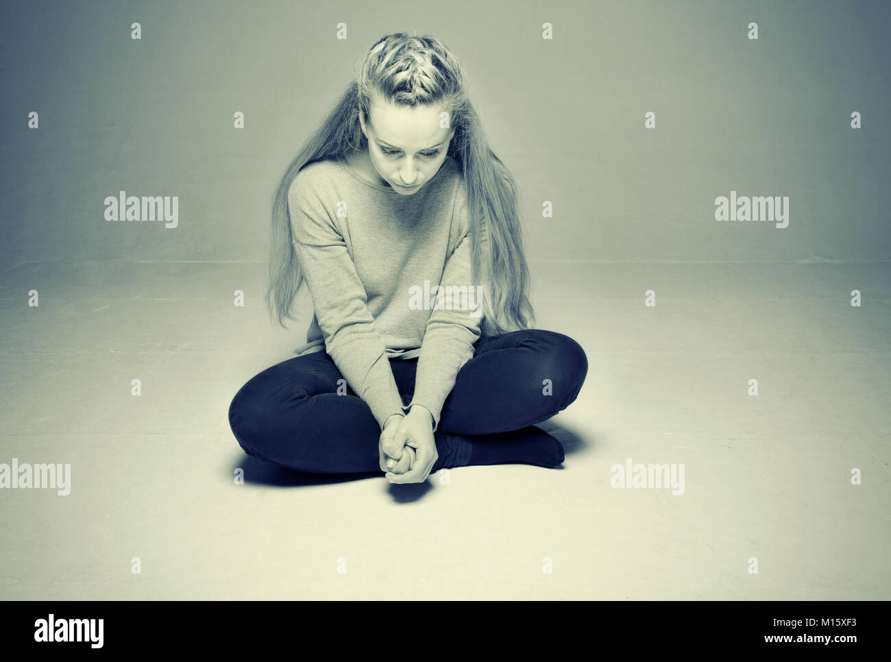 Traurige Frau im leeren zimmer sitzen auf dem Boden Beine Hände gekreuzt fest umklammert vor, getönten Bild gedrückt Stockfoto