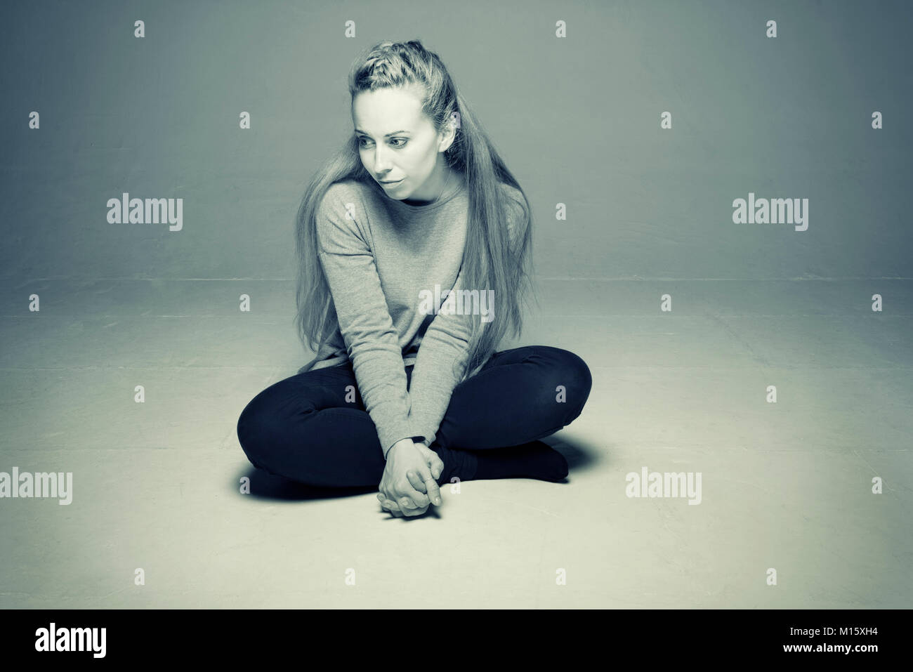 Traurig, deprimiert Frau sitzt im leeren Raum auf dem Boden Beine dicht vor gekreuzt vors weit weg auf der Suche am Boden getonten Bild Stockfoto