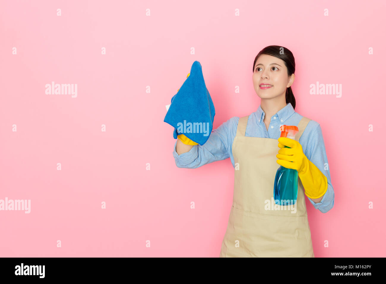 Attraktive lächelnd weibliche houseworker Holding Reinigungsmittel Flasche reinigen Glas Fenster und mit rag-tool auf rosa Hintergrund isoliert zu wischen. Stockfoto