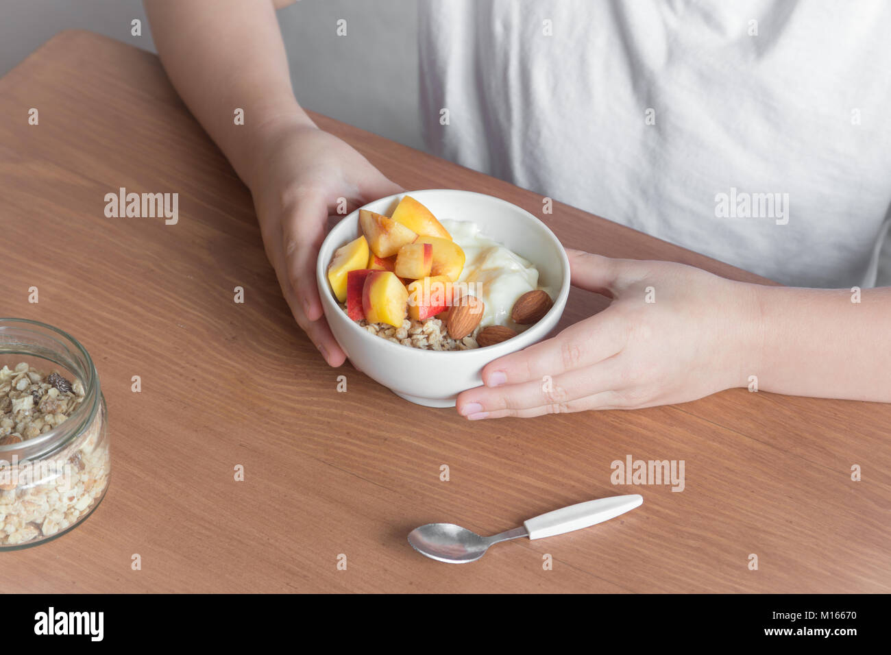 Gesund essen Frühstück Schüssel. Haferflocken Müsli, Joghurt, frische Nektarinen inweiß Schüssel in weiblich (Kind) Hände über Holz- Tabelle. Sauber, Essen, Diät Stockfoto