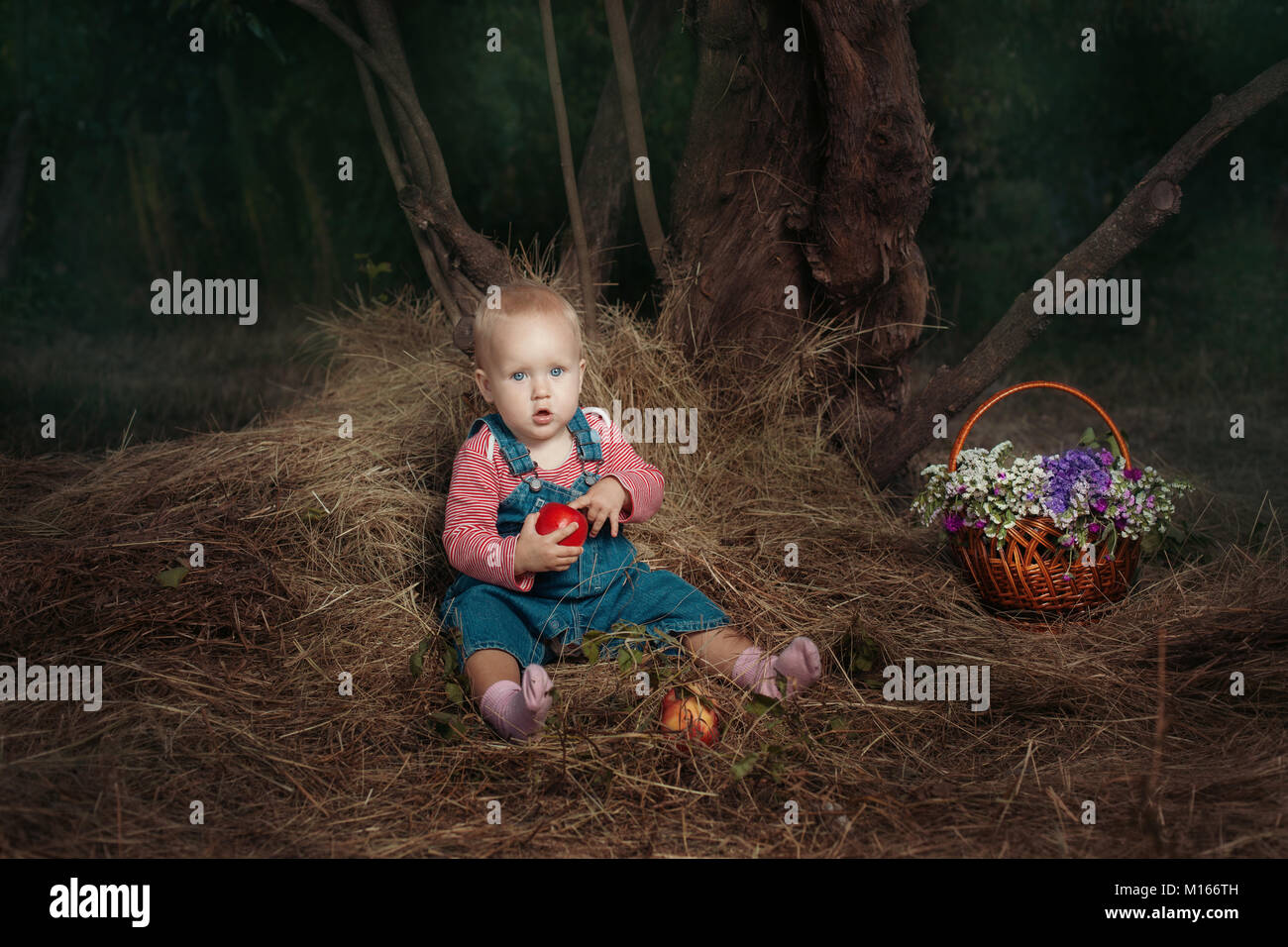 Kleines Mädchen saß unter einem Baum und mit einem Apfel. Stockfoto