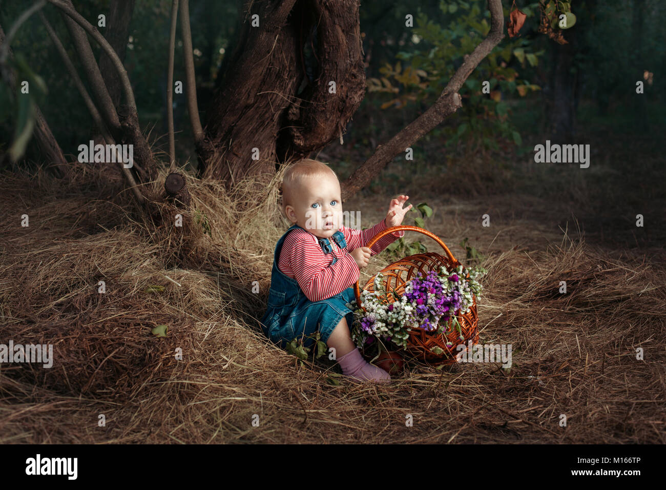 Kleines Mädchen mit einem Korb mit Blumen sitzen unter einem Baum. Stockfoto