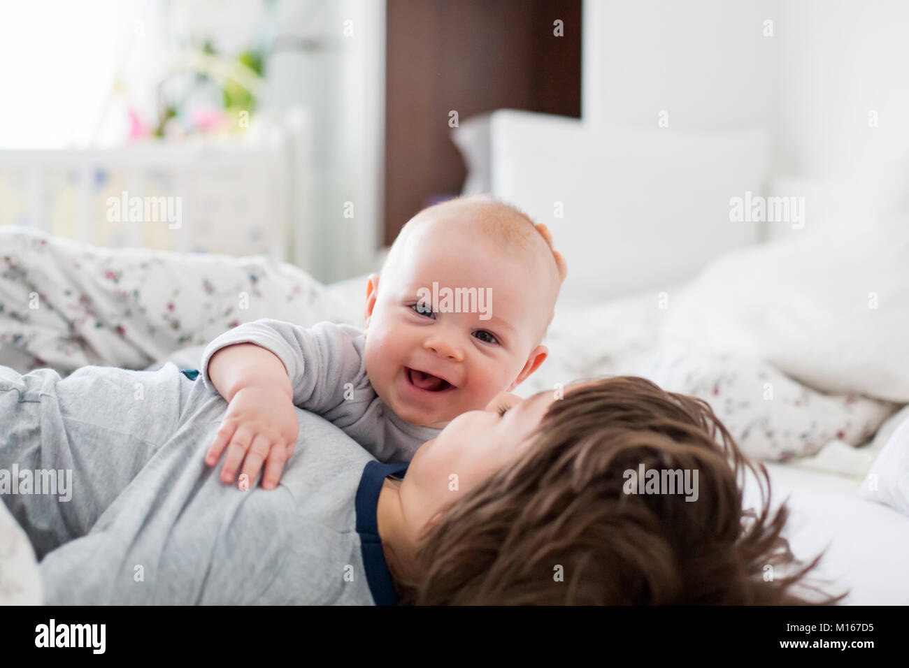 Zwei Kinder, Baby und sein älterer Bruder im Bett am Morgen, gemeinsam spielen, lachen und eine gute Zeit, die gemeinsame Nutzung von speziellen Moment, Kleben Stockfoto
