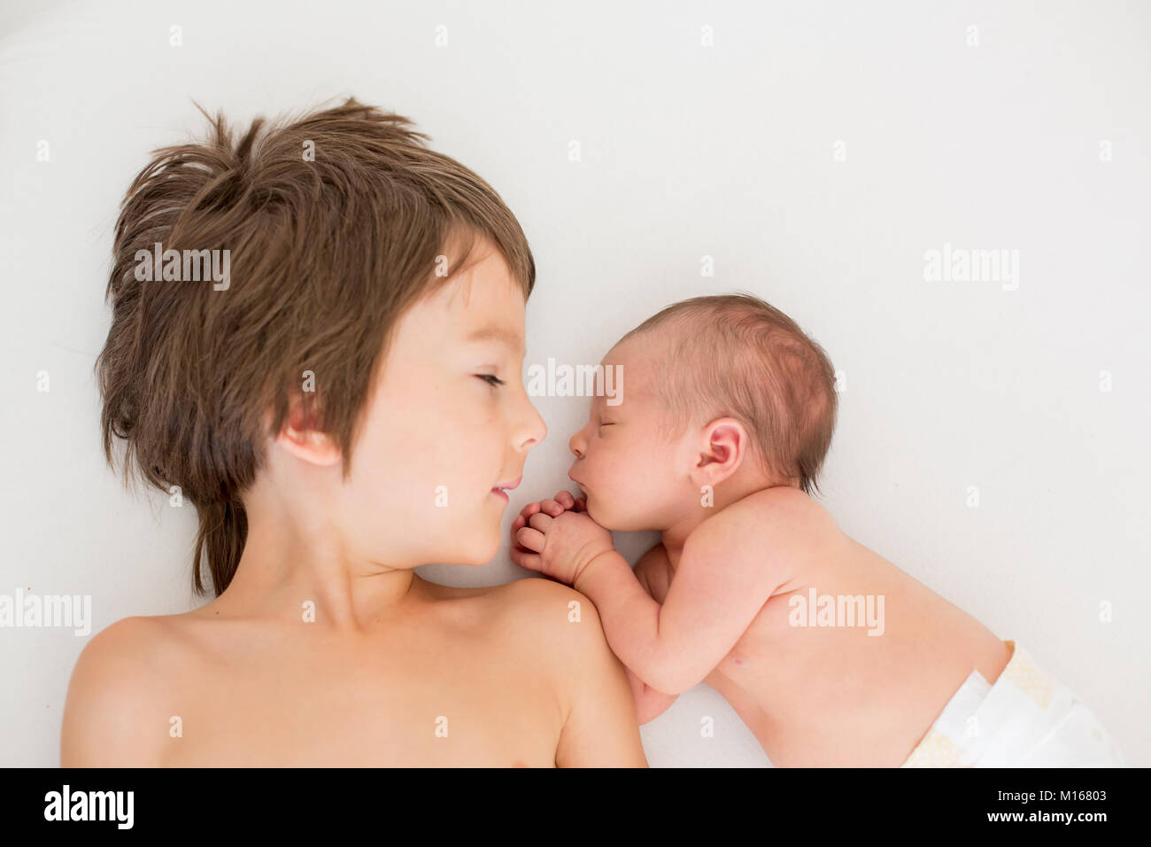 Schöne junge, umarmen mit Zärtlichkeit und sein neugeborenes Baby Bruder Pflege zu Hause. Familie Liebe Glück Konzept Stockfoto