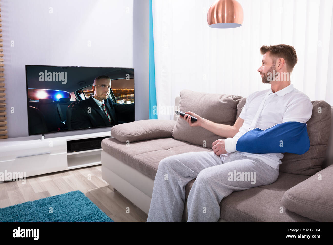 Junger Mann mit gebrochenen Hand sitzen auf dem Sofa anschauen Film zu Hause im Fernsehen Stockfoto