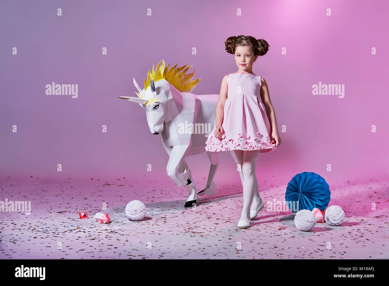 Romantisches kleines Mädchen in schönen rosa Kleid. Origami und Minimalismus. Mode Kinder. Designer Kollektion. Weiß groß Einhorn origami aus Papier. Stockfoto