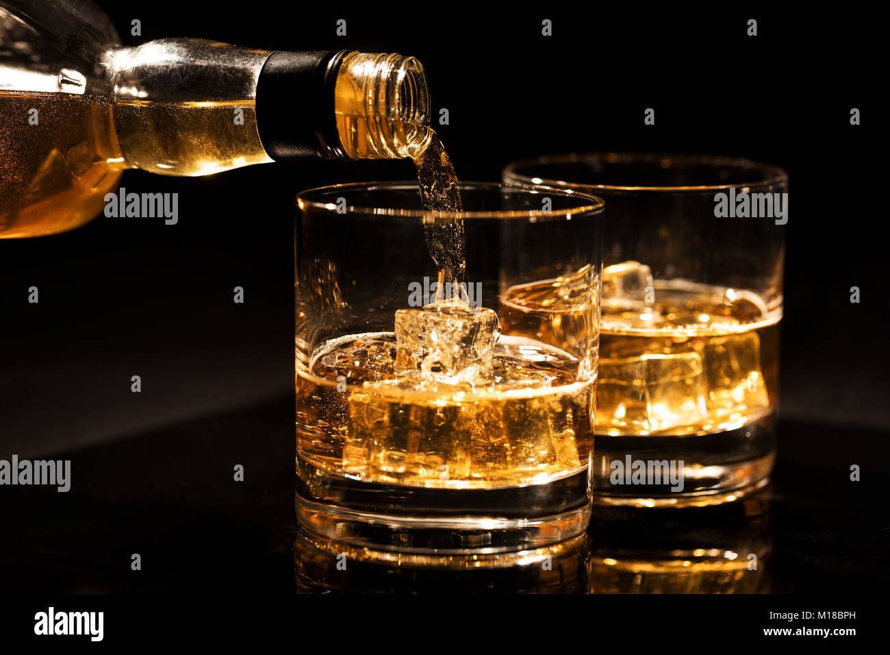 Gießt Whiskey von der Flasche in ein Glas mit Eiswürfeln auf schwarzem Hintergrund Stockfoto