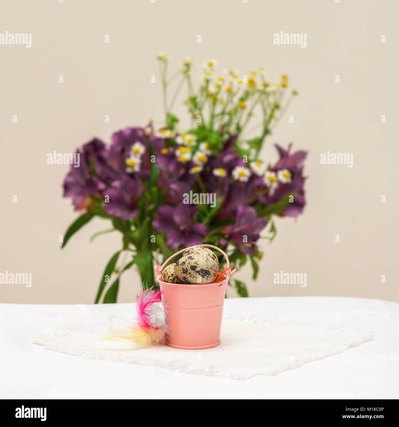 Natürliche Wachteleier in kleinen rosa Eimer, bunten Federn vor Violett Blumen, leicht rustikal Serviette auf dem Tisch, selektive konzentrieren. Ostern, Frühling, biologische Lebensmittel, Ernährung Stockfoto