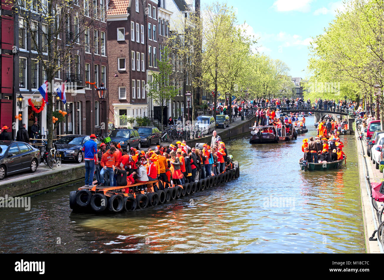 Eine Szene auf einem Kanal in Amsterdam auf des Königs Tag. Mehrere Boote im Kanal alle voller feiern Menschen tragen orange Farbe der Kleidung. Stockfoto