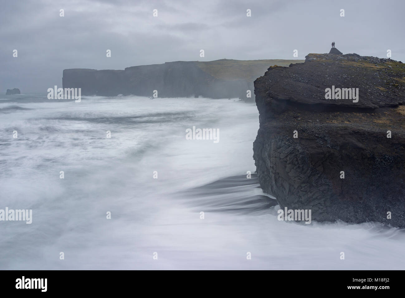 Paar steht oberhalb der Klippen von Dyrholey bei Sturm, Vik, Rangárvallahreppur, Iceland Stockfoto