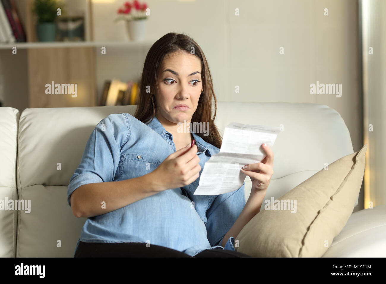 Misstrauisch schwangere Frau Lesen einer Packungsbeilage vor nehmen Sie eine Pille sitzen auf einer Couch im Wohnzimmer zu Hause Stockfoto